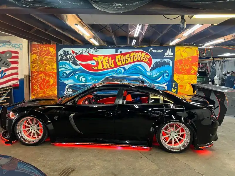 Black widebody Dodge Charger with red LED underglow and lit wheel rings in front of the TRU Customs mural