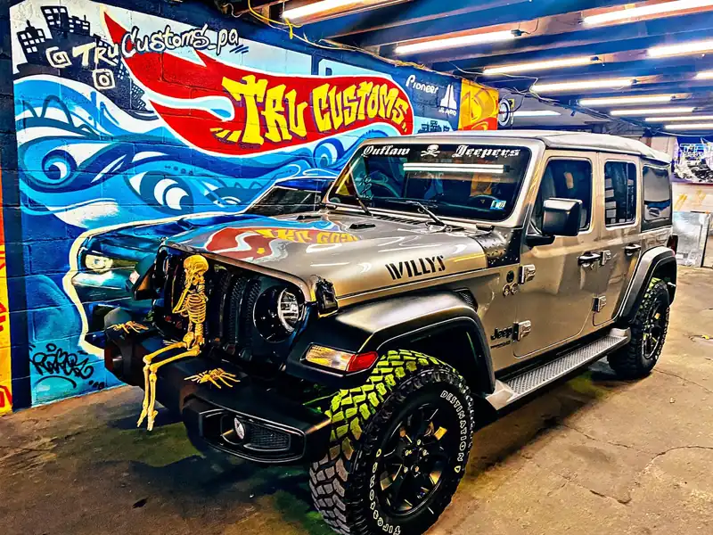 Silver Jeep Wrangler Willys with off-road tires and a windshield banner